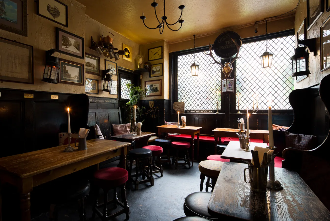 Empty pub snug with candlelit wooden tables, red stools, framed pictures and leaded windows.